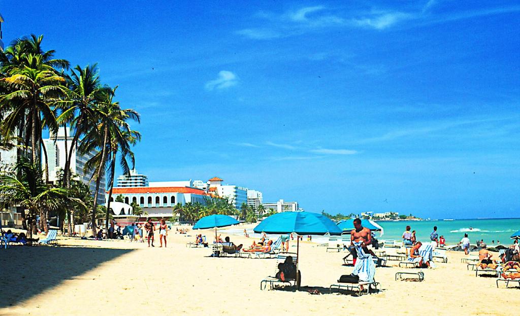 un groupe de personnes sur une plage avec des parasols bleus dans l'établissement Canario Boutique Hotel, à San Juan