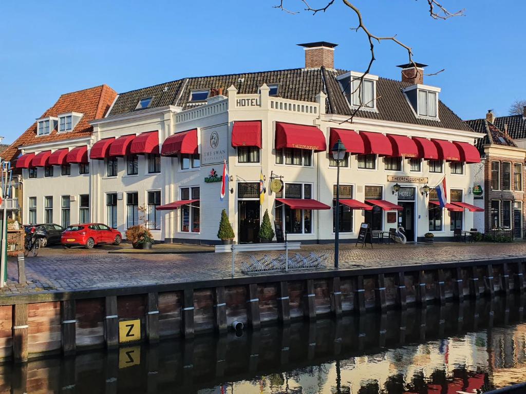 a building with red awnings next to a river at Hotel Restaurant 't Heerenlogement in Harlingen