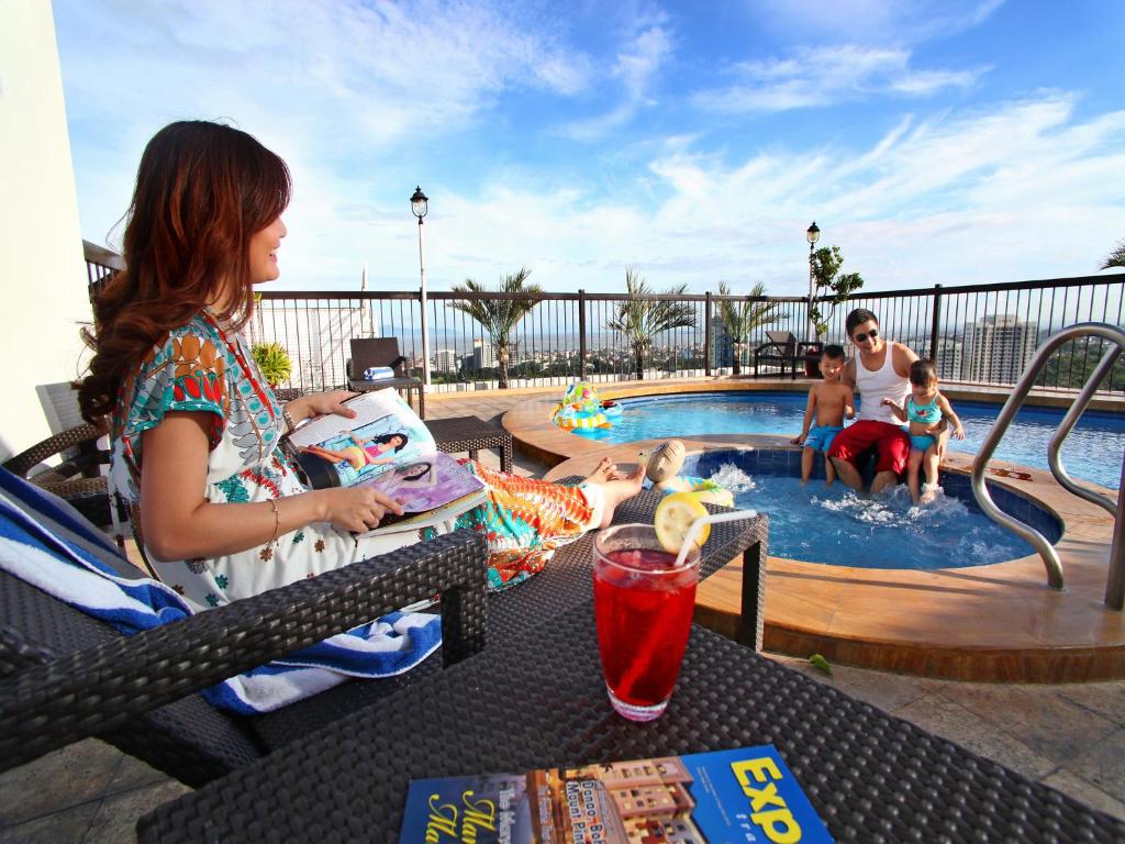 Parque España Residence Hotel Managed by HII في مانيلا: امرأة تجلس على طاولة أمام مسبح