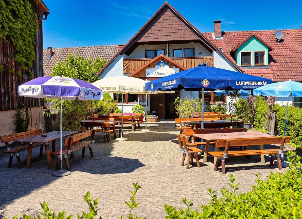 un patio con mesas de madera y sombrillas frente a un edificio en Zur Altmühlquelle, en Windelsbach