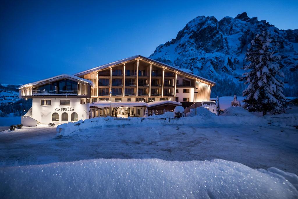 a large building with snow in front of a mountain at Hotel Cappella in Colfosco