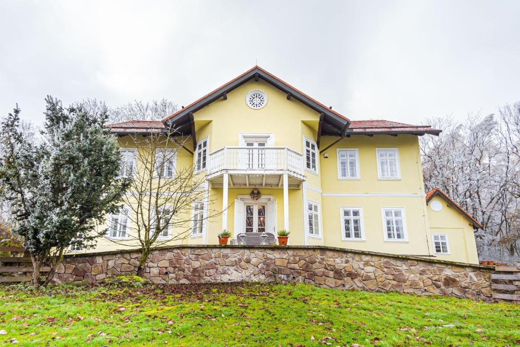 een geel huis bovenop een stenen muur bij Lovecký zámeček pod Milešovkou in Teplice