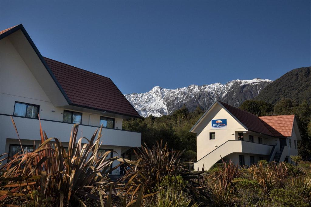 a house and a building with mountains in the background at Bella Vista Motel Fox Glacier in Fox Glacier