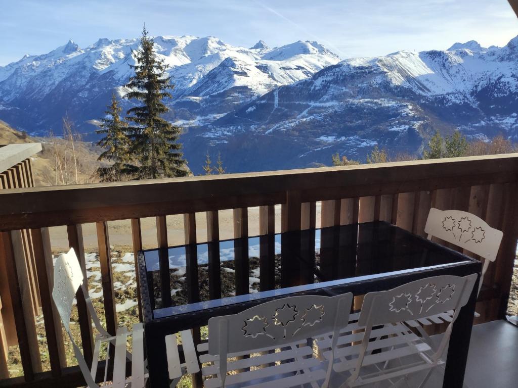 a table and chair on a balcony with snow covered mountains at Les Iris T2 station Alpe Huez in Auris