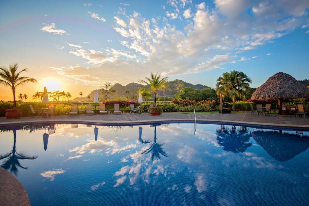 a pool at a resort with the sun setting at Ocean View Condo in Los Sueños in Herradura