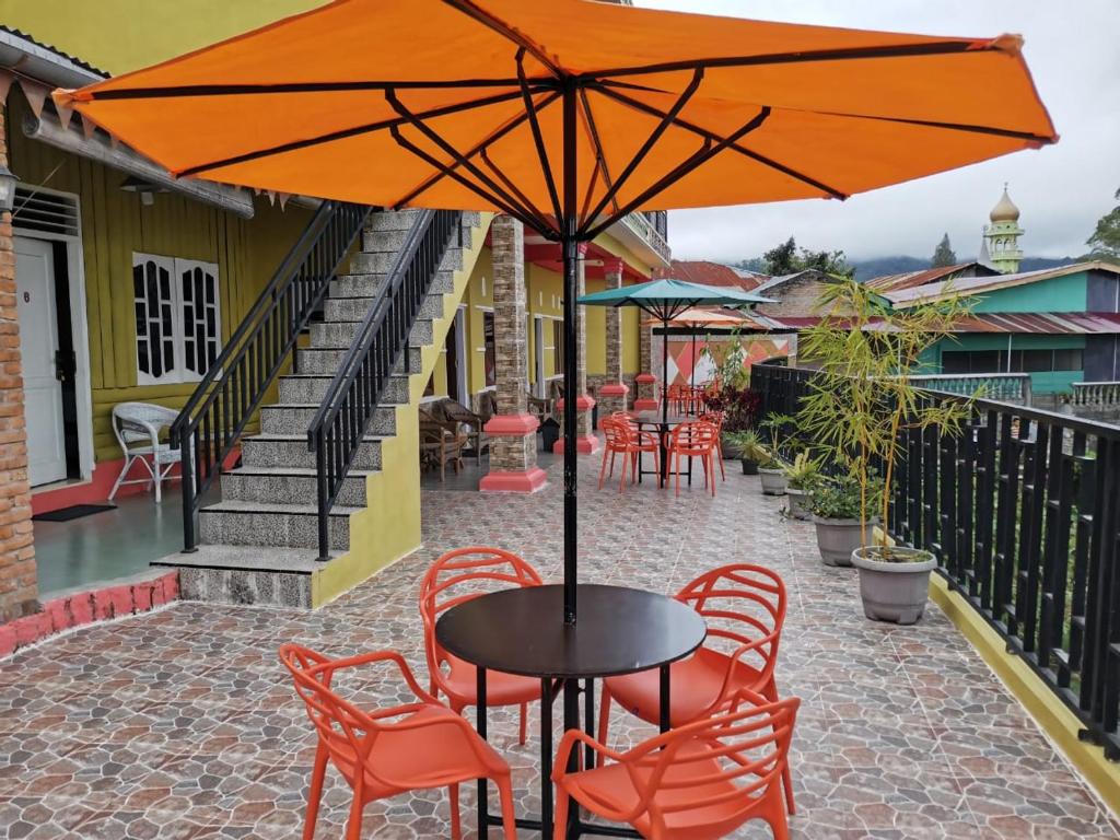 una mesa con sillas naranjas y una sombrilla en el patio en WELCOME TO WISMA SUNRISE GUEST HOUSE 10 minutes by walking to the big fruit market, en Berastagi