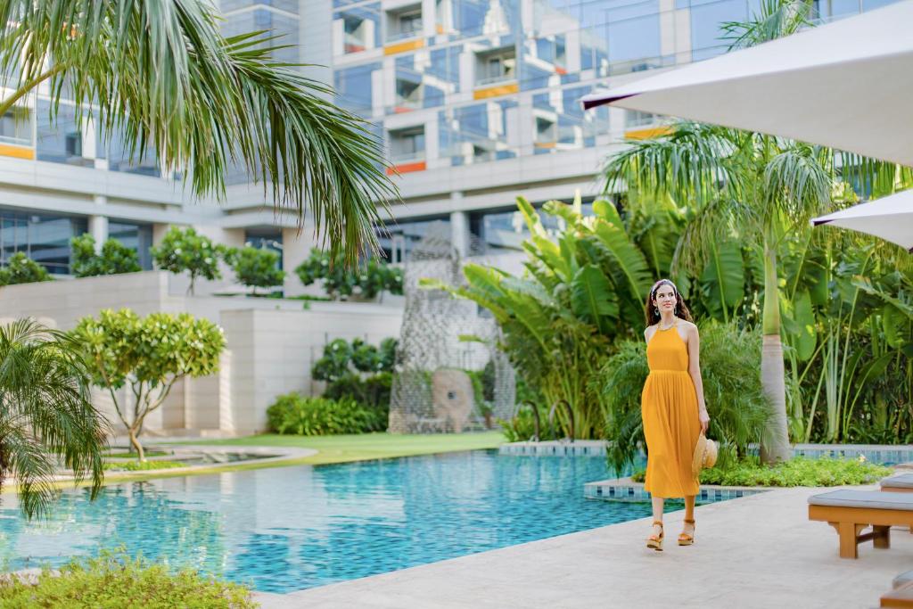 una mujer con un vestido amarillo de pie junto a una piscina en Andaz Delhi Aerocity- Concept by Hyatt en Nueva Delhi