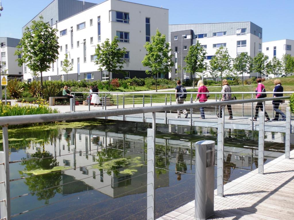 Gente caminando sobre un puente sobre un estanque en una ciudad en Queen Margaret University Residences, en Musselburgh