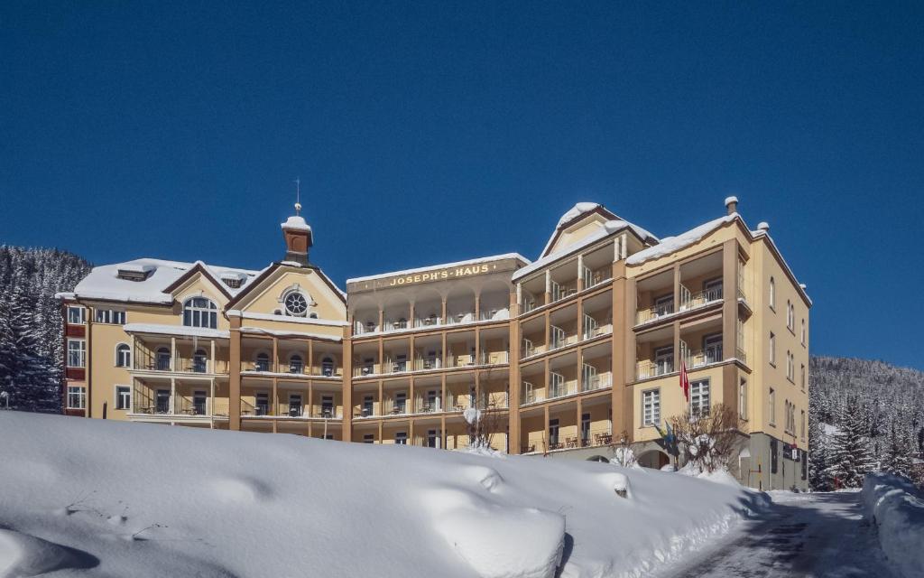 un grand bâtiment avec de la neige devant lui dans l'établissement Hotel Joseph's House, à Davos