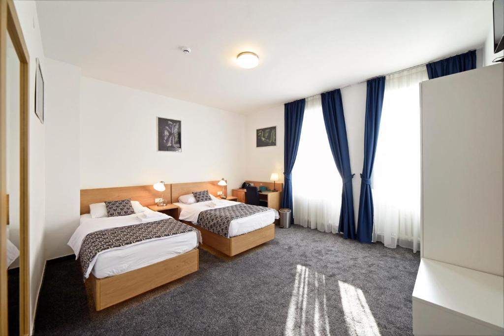 two beds in a room with blue curtains at Hotel Orient Zagreb in Zagreb