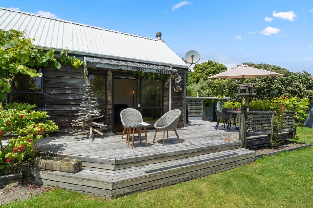 a wooden deck with chairs and an umbrella at Waimea Cottage - Waikanae Holiday Home in Waikanae