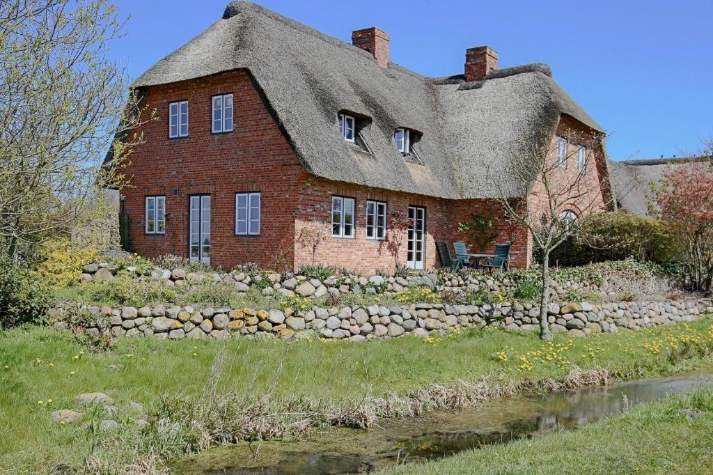 ein altes Backsteinhaus mit einem Strohdach neben einem Teich in der Unterkunft Reethus Jan in Husum