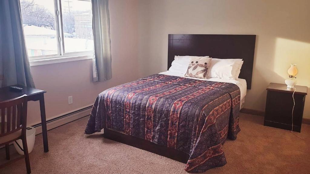 a bedroom with a bed with a blanket and a window at BUDGET LODGE in Saskatoon