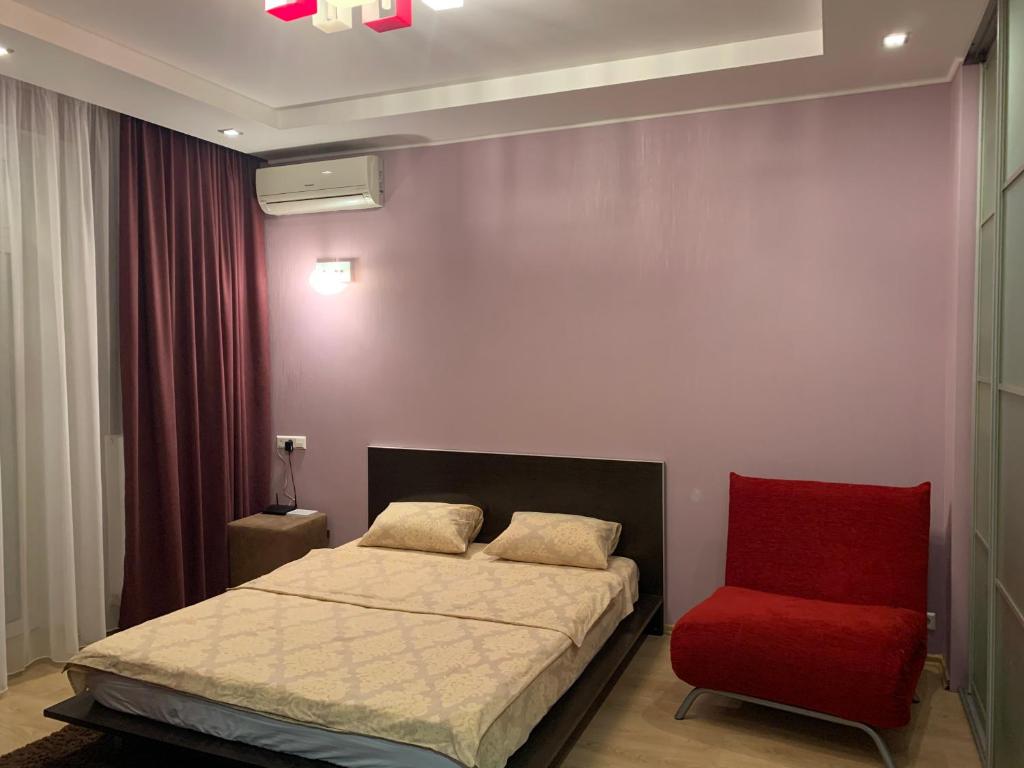 - une chambre avec un lit et une chaise rouge dans l'établissement Квартира, à Dnipro