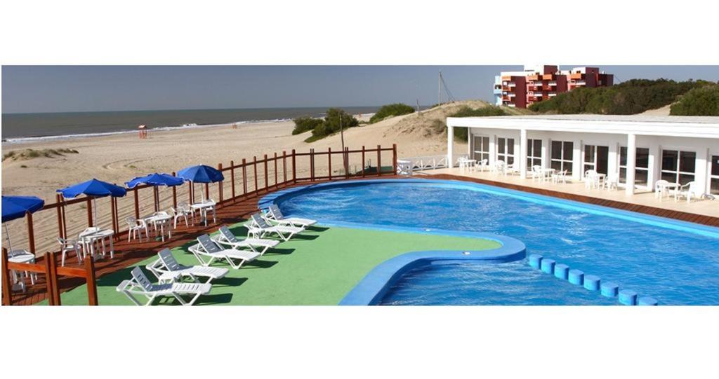 una piscina junto a una playa con sillas y sombrillas en Terrazas Playa, en Villa Gesell