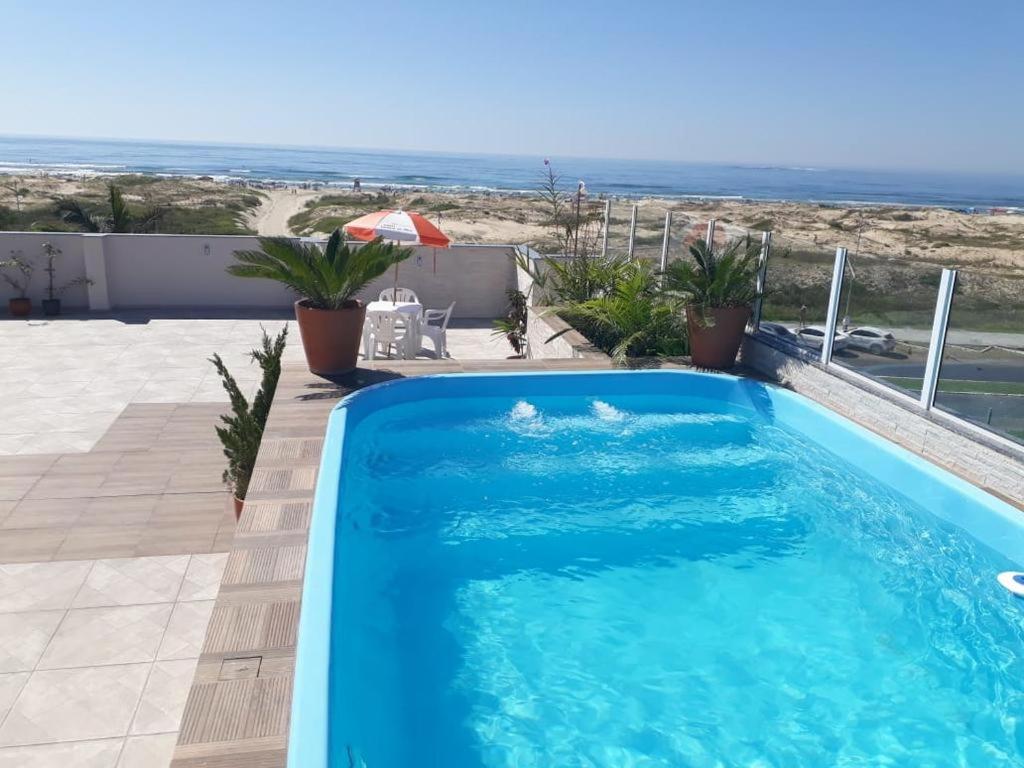 a blue swimming pool with a view of the beach at Hotel Jardim do Mar in Torres