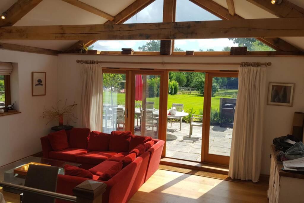a living room with a red couch and a sliding glass door at 4 Kingsize Beds Ensuite - Sleeps 8-10 - Rural Contemporary Oak Framed House in Chiddingfold