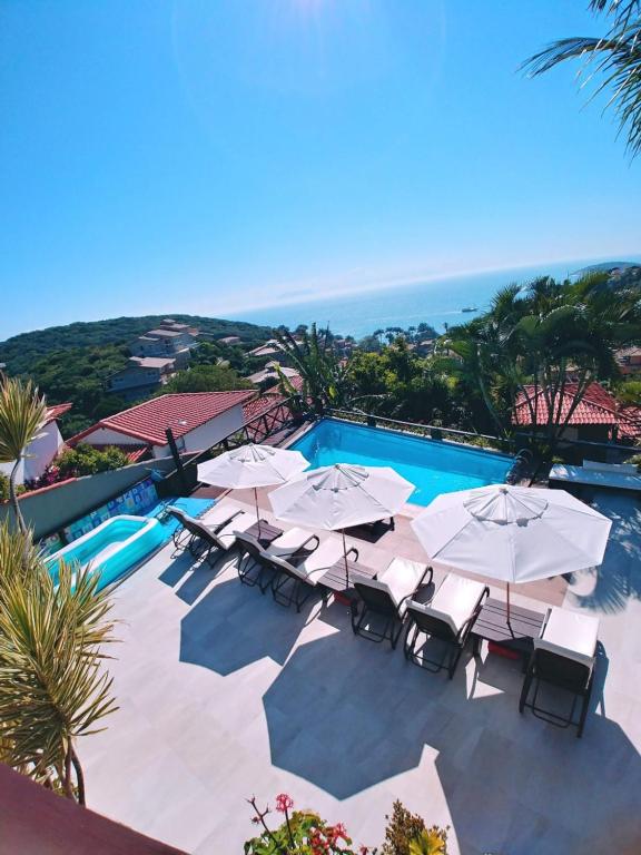 uma piscina com guarda-sóis e cadeiras e o oceano em Pousada Vila do Sol em Búzios