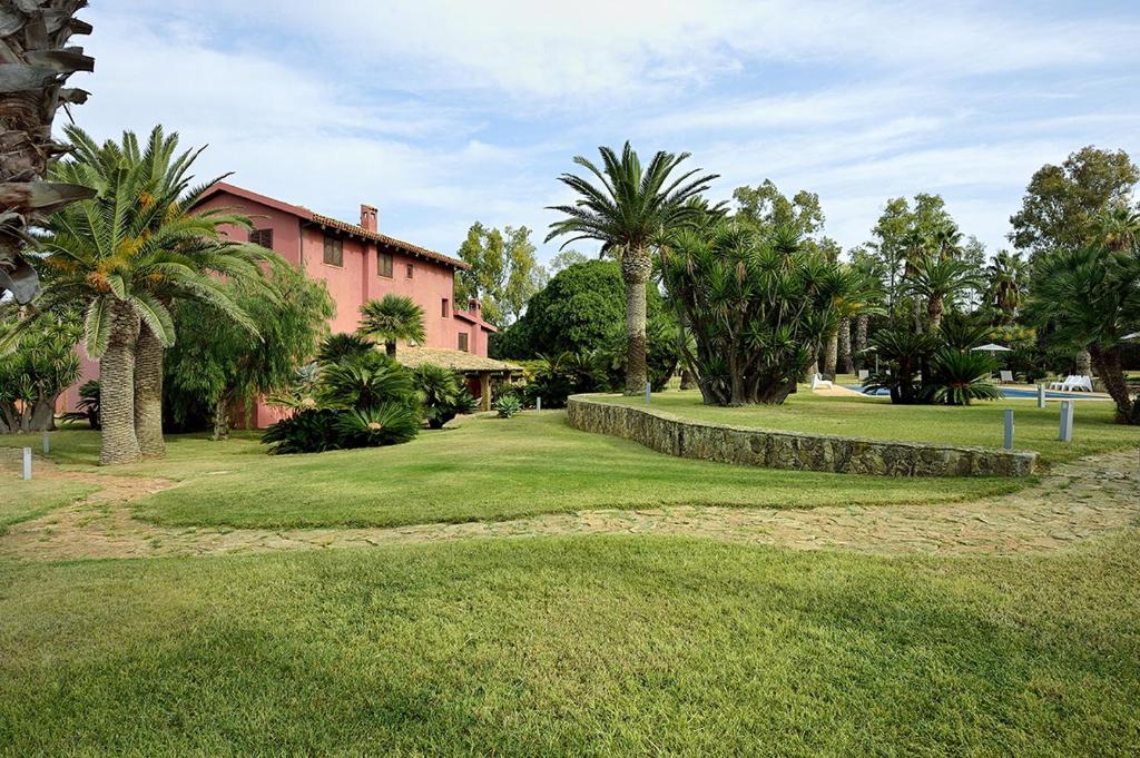 un parc avec des palmiers et un bâtiment rose dans l'établissement Casa Realia, à Agrigente