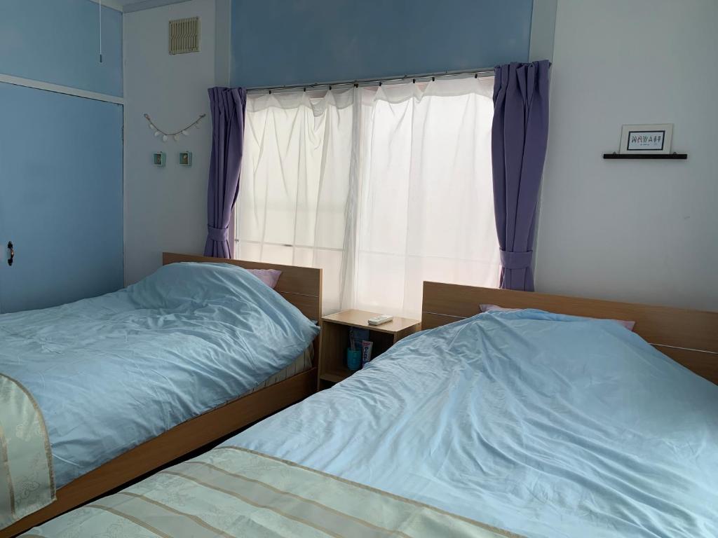 a bedroom with two beds and a window with purple curtains at Cozy Penguin House Bibai in Bibai