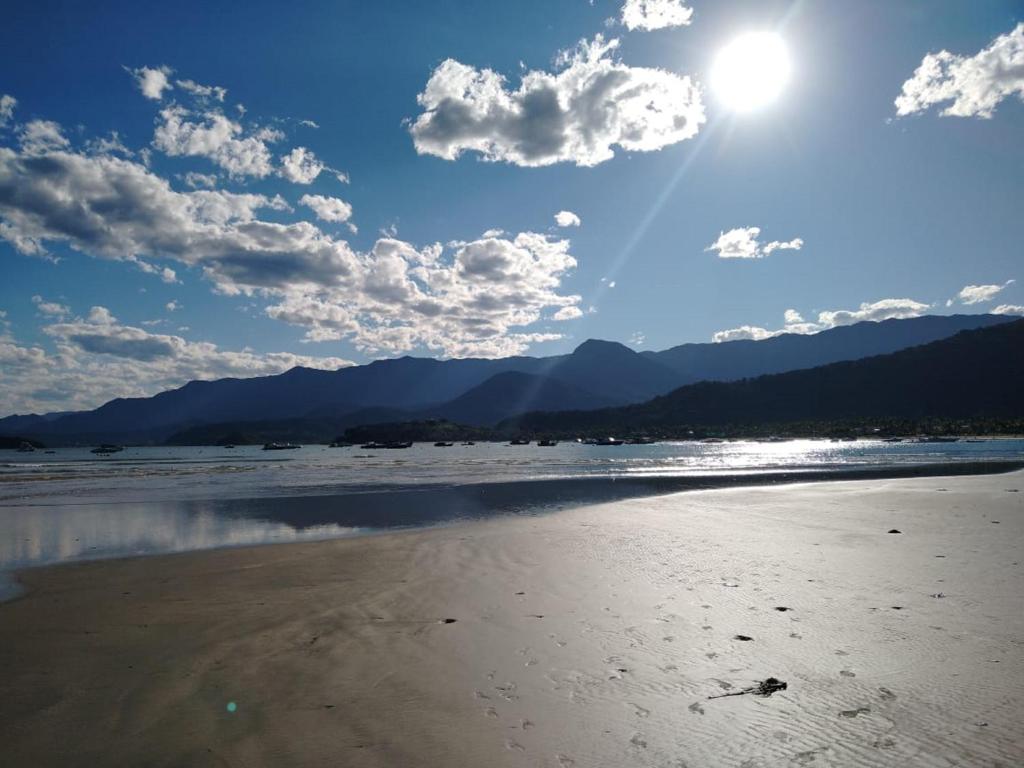 uma praia com sol e montanhas ao fundo em Praialar Apartamentos Ubatuba em Ubatuba