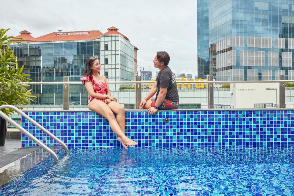 a man and a woman sitting on the edge of a swimming pool at ibis budget Singapore Clarke Quay in Singapore