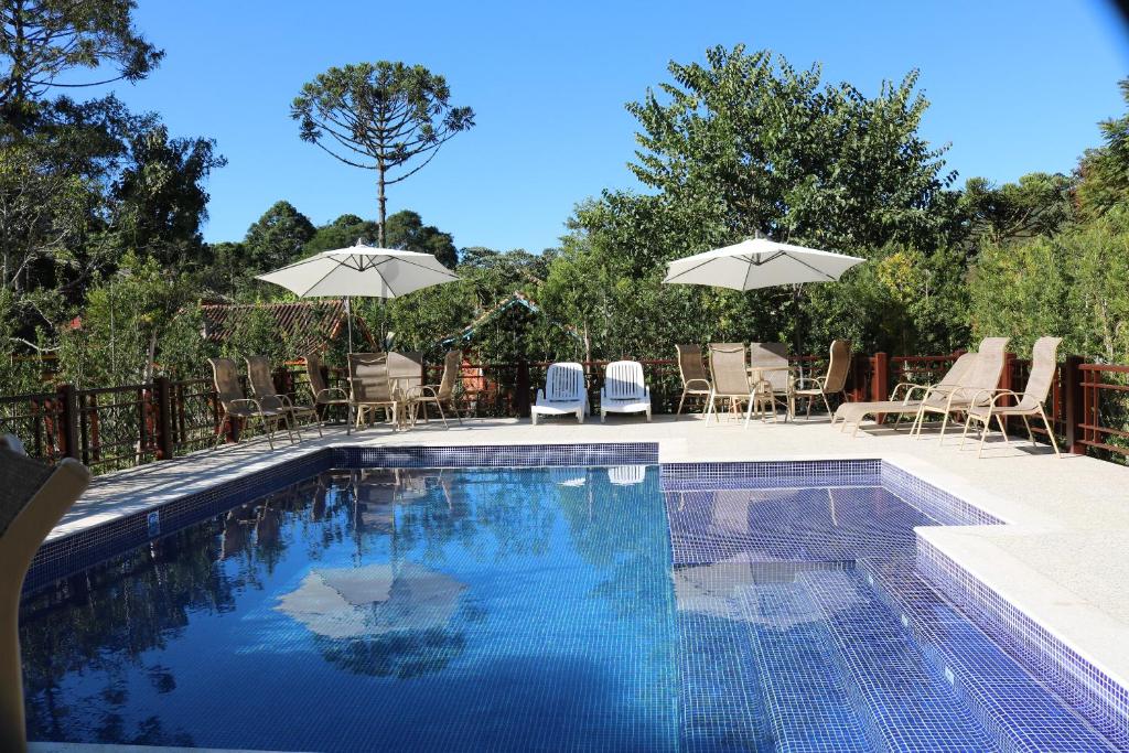 una piscina con mesas, sillas y sombrillas en Pousada Jardim da Luz en Visconde De Maua