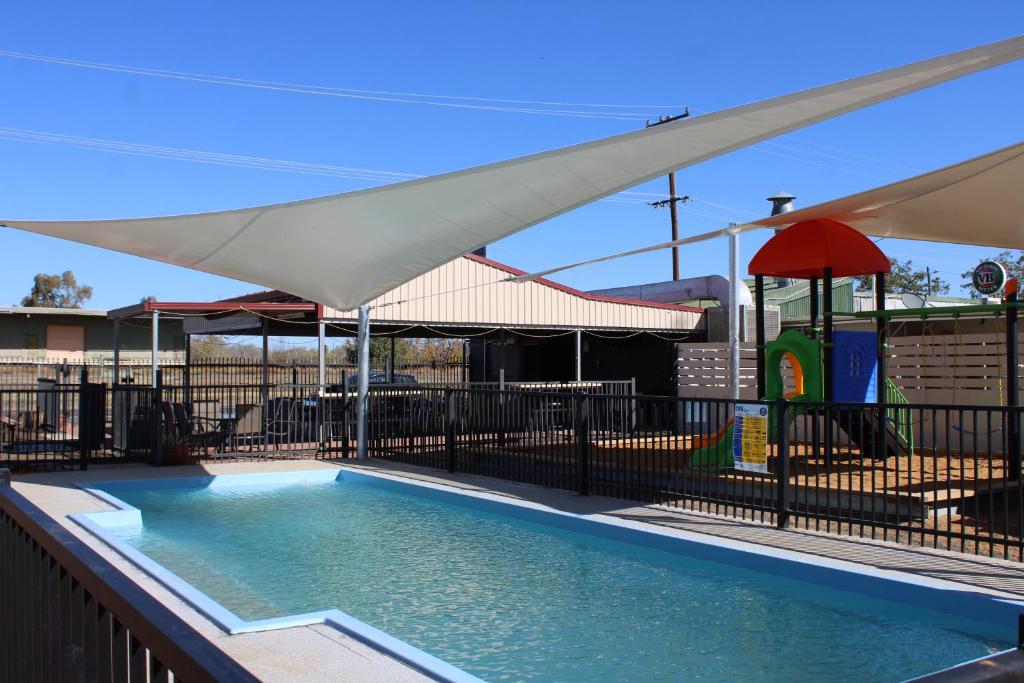 a swimming pool with an umbrella and a playground at Sunshine Gardens Bourke Resort in Bourke