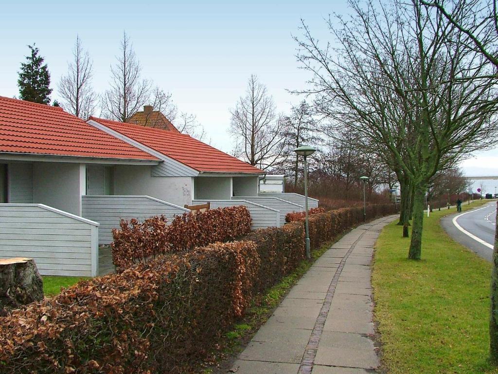 a hedge fence next to a house and a sidewalk at 4 person holiday home in r sk bing in Ærøskøbing