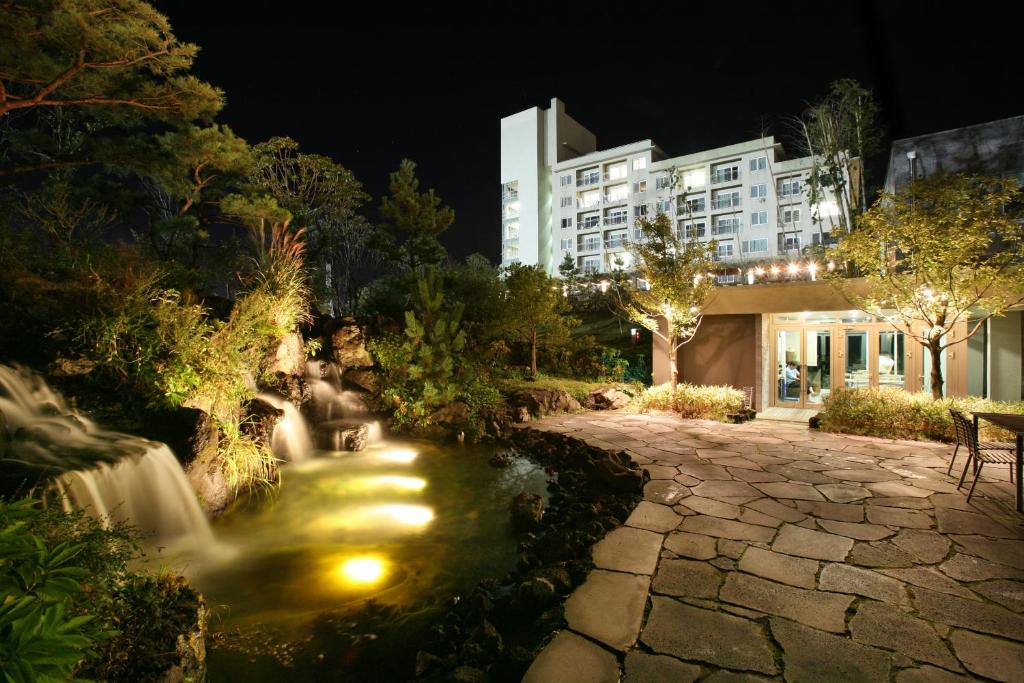 - un jardin de nuit avec une cascade et un bâtiment dans l'établissement Hanwha Resort Jeju, à Jeju