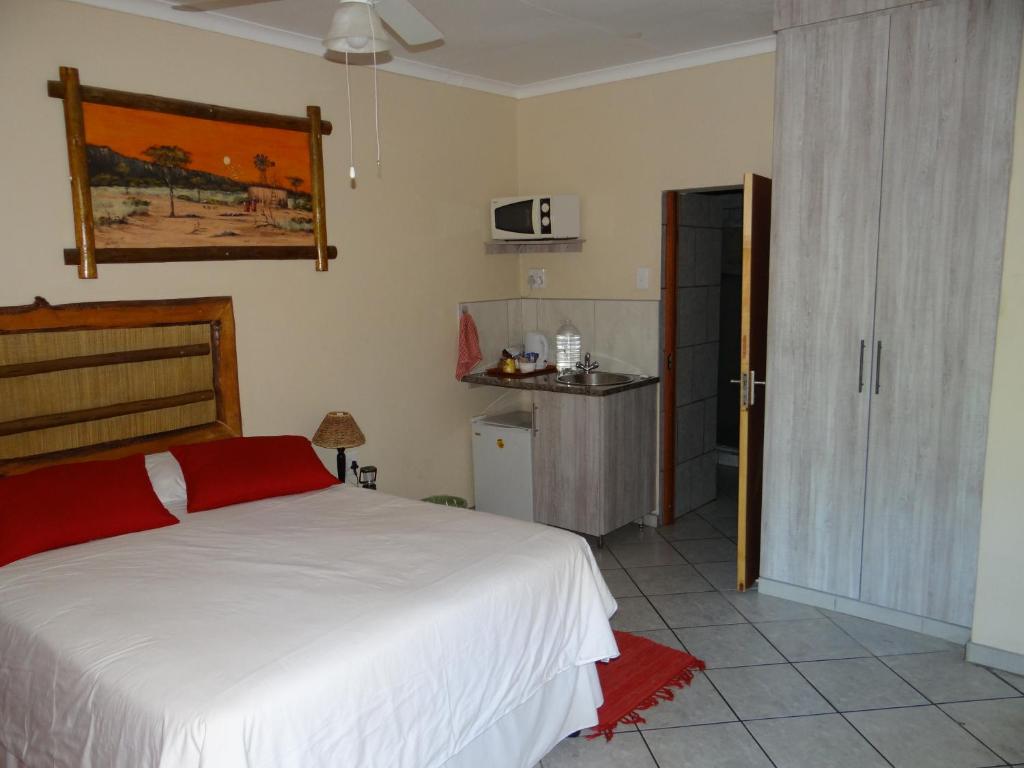 a bedroom with a white bed and a kitchen at Lephalale Guest House in Ellisras
