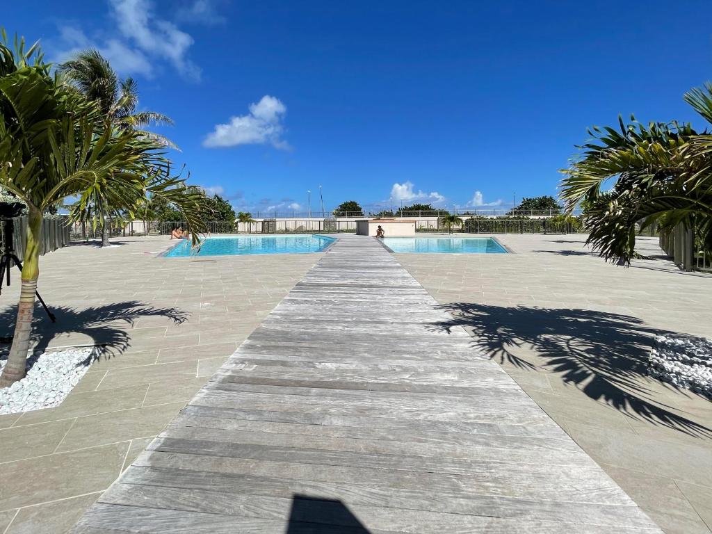 a wooden pathway leading to a swimming pool with palm trees at Orient Bay Beach Front Apartment in Orient Bay