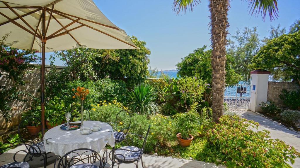 a table and chairs with an umbrella in a garden at Villa Beach House Orebic with private pool at the beach in Orebic - Peljesac in Orebić
