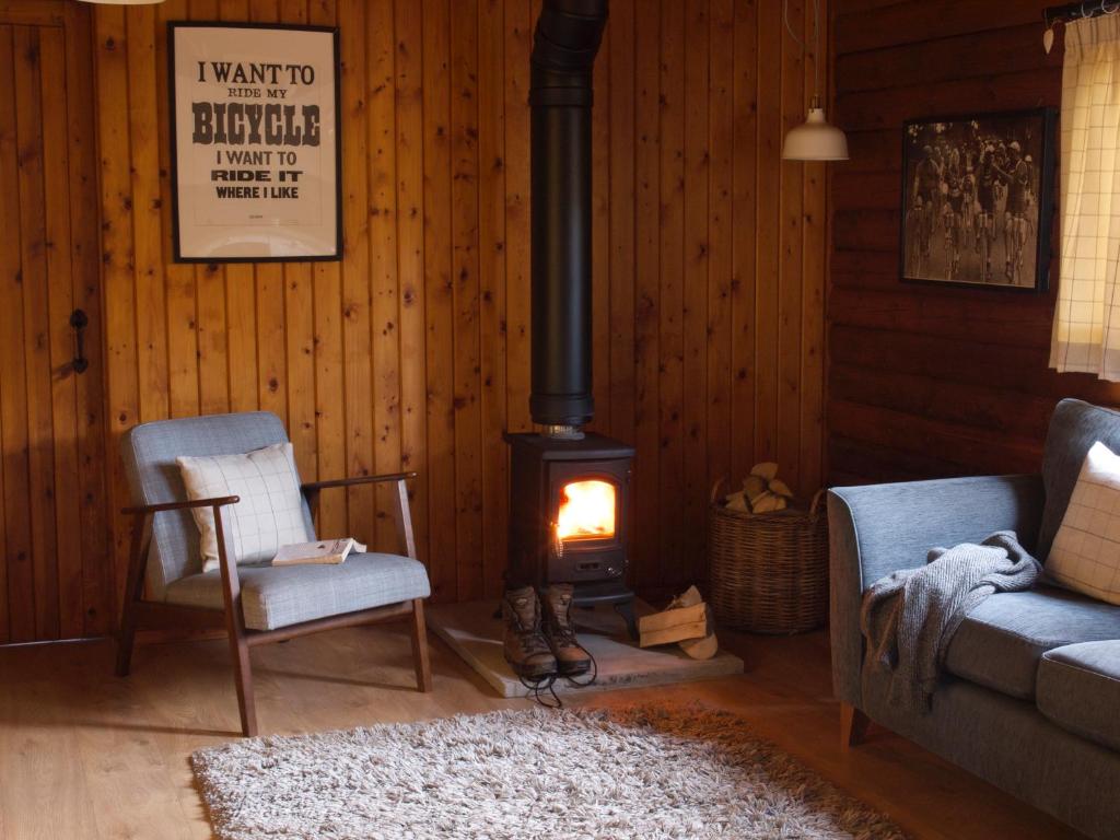 een woonkamer met 2 stoelen en een houtkachel bij Hillside Log cabin, Ardoch Lodge, Strathyre in Strathyre