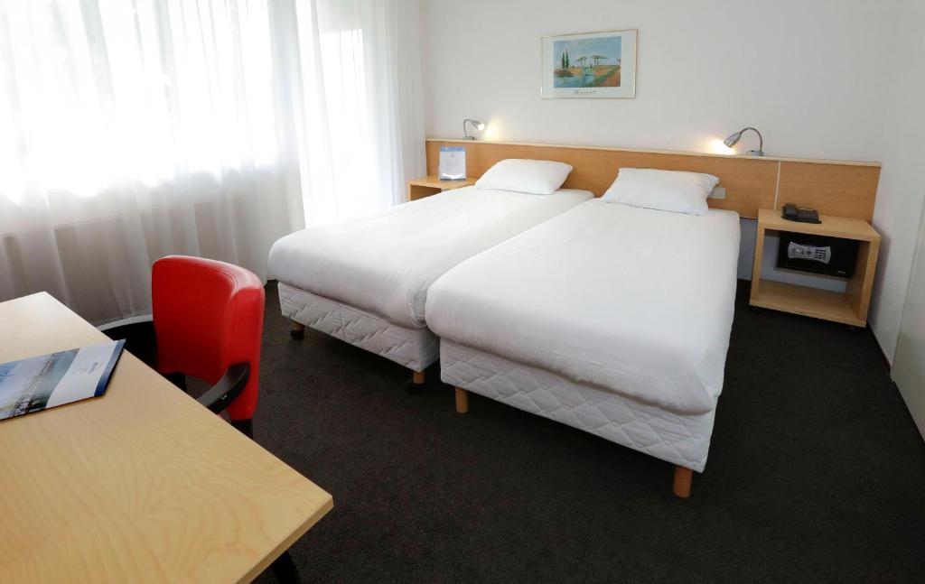 a hotel room with two beds and a red chair at City hotel Terneuzen in Terneuzen