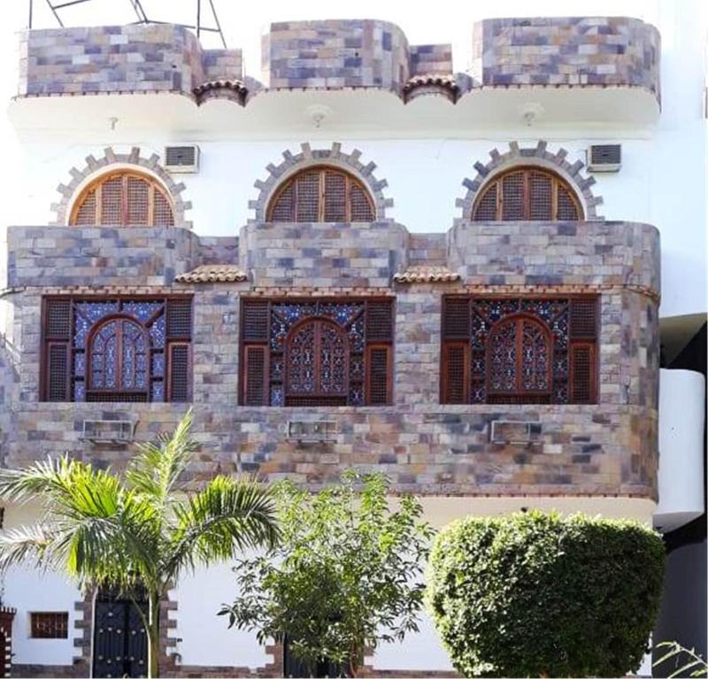 a building with three windows and palm trees in front at Arabesque House Apartment in Luxor