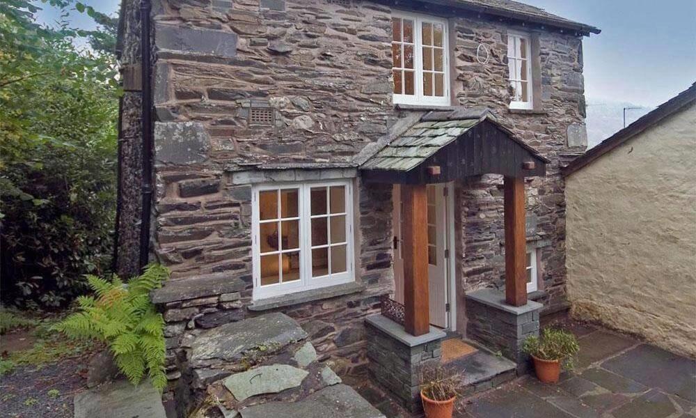 an old stone house with white windows and doors at Ivy Cottage in Ambleside