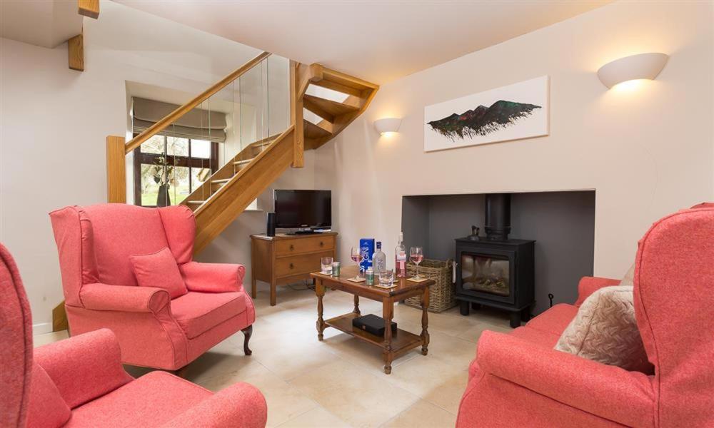 a living room with red chairs and a staircase at Barn Cottage in Cockermouth