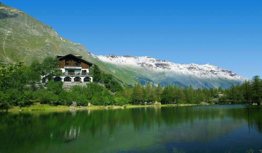 une maison sur la rive d'un lac en face d'une montagne dans l'établissement Chalet Sul Lago Hotel In Montagna, à Moncenisio