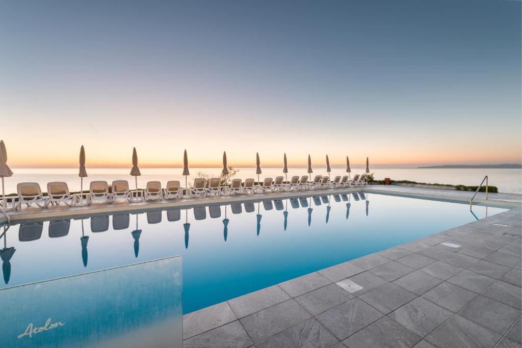 una piscina con sillas y el océano en el fondo en Hotel Atolon, en Cala Bona