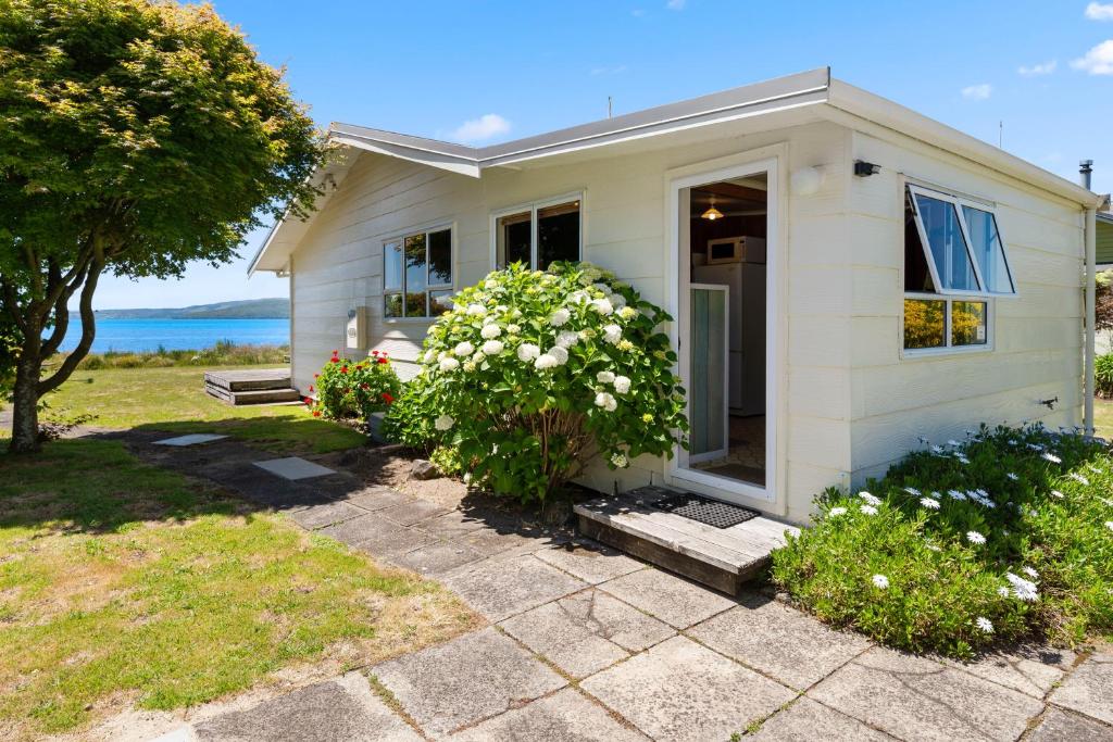 une petite maison blanche avec une brousse devant elle dans l'établissement The Lake Bach - Ngongotaha Lakefront Holiday Home, à Ngongotaha