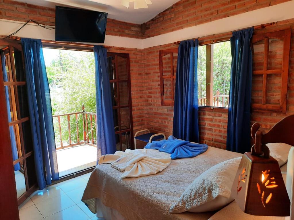 1 dormitorio con 1 cama con cortinas azules y TV en Departamentos Los Álamos en Mina Clavero