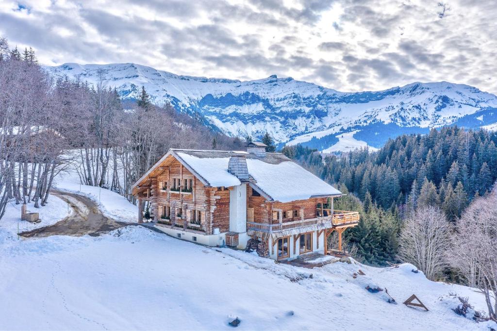une cabane en rondins dans la neige avec des montagnes en arrière-plan dans l'établissement Chalet Les Meuniers, à Megève