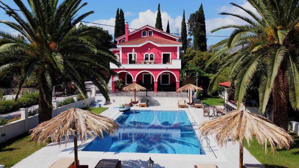 a large pink house with a swimming pool and palm trees at Zissis Villa & pool 5min drive to beach in Káto Yerakaríon