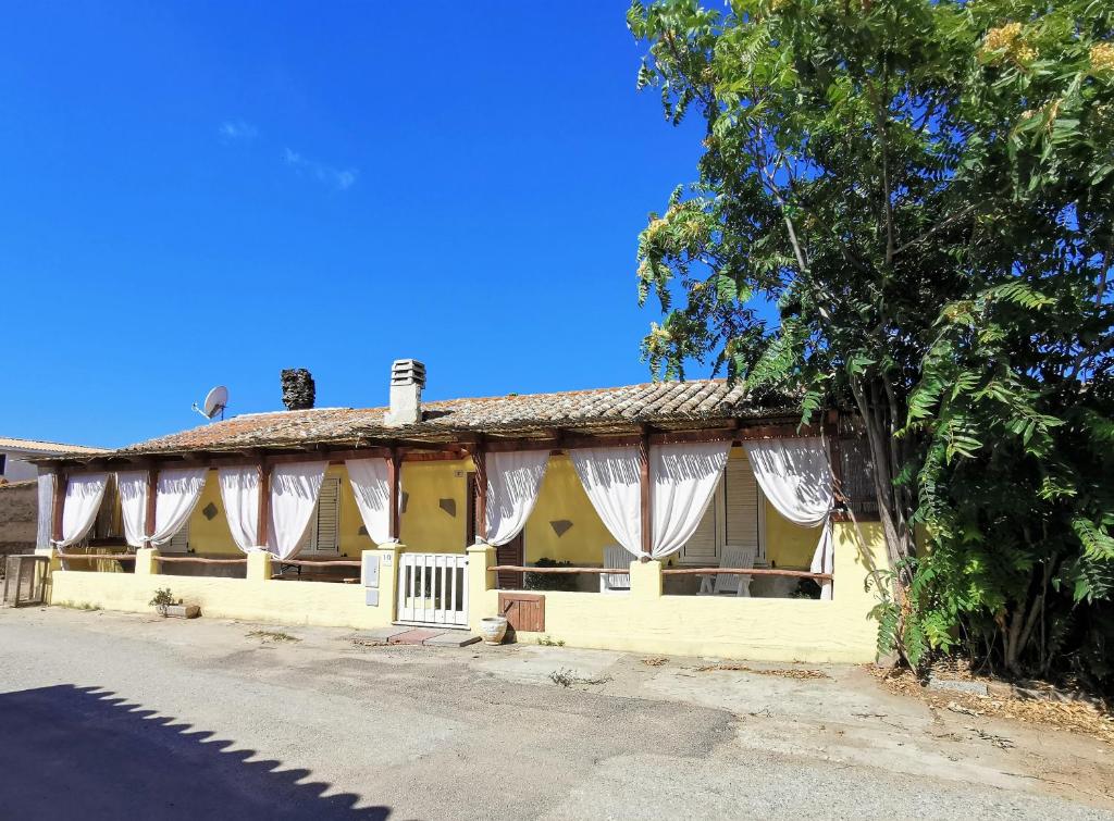 ポルト・ピノにあるVilla Sandraの白いカーテンと木のある黄色い家