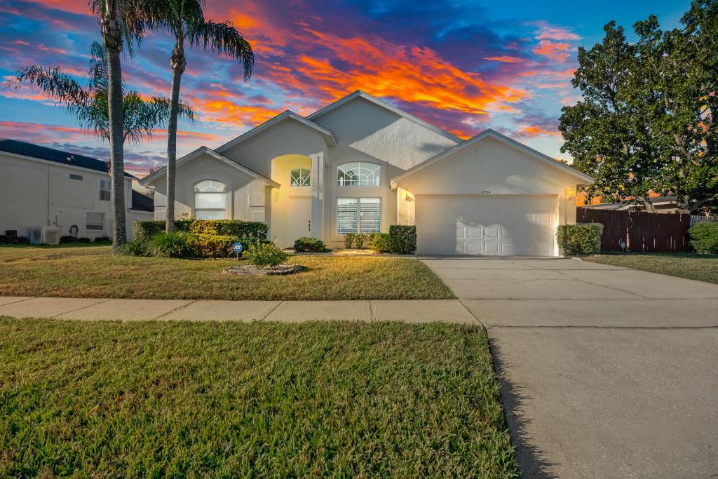 a white house with a palm tree and a sunset at Quiet Home With Private Pool- Near Disney in Kissimmee