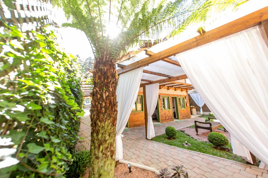 un patio al aire libre con cortinas blancas y un árbol en Pousada Charm Canela, en Canela