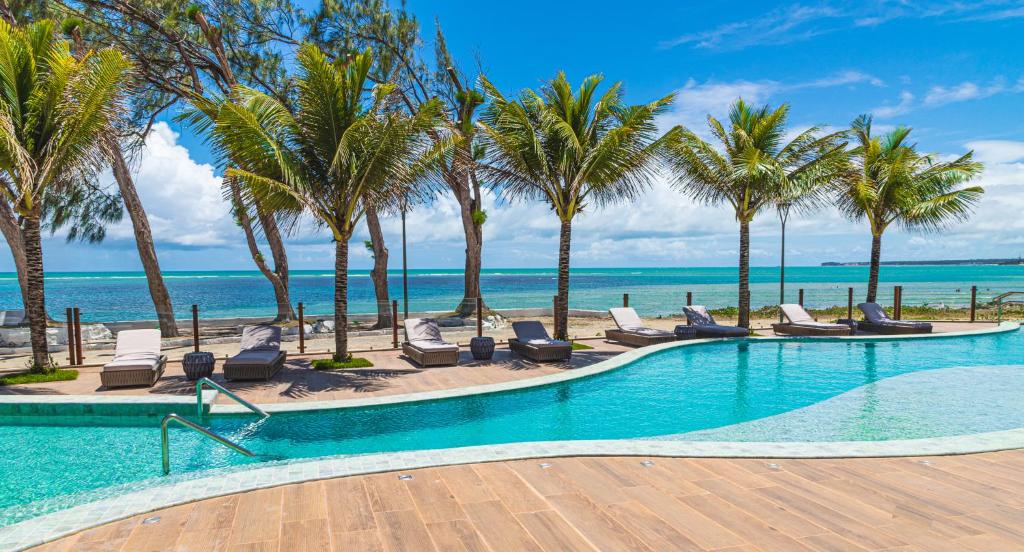 uma piscina com palmeiras e cadeiras e o oceano em Oceana Atlântico Hotel em João Pessoa