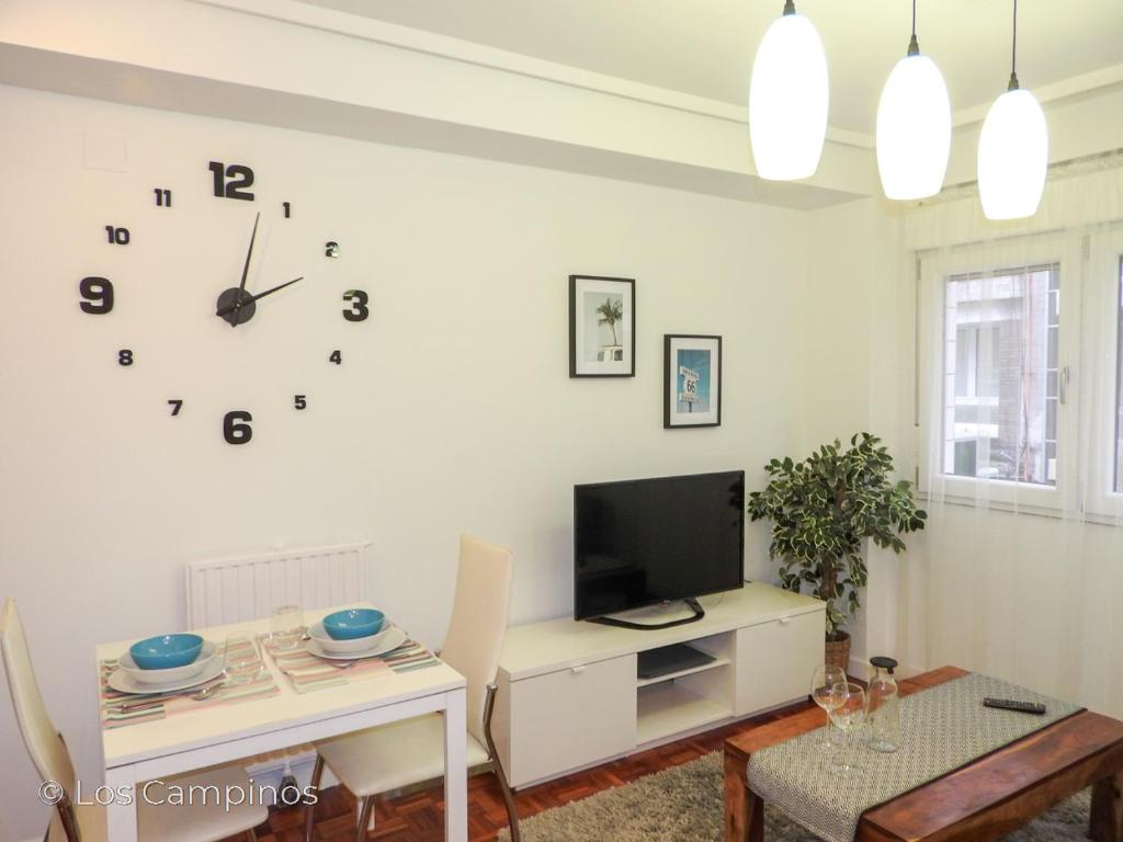 uma sala de estar com televisão e um relógio na parede em Los Campinos - Pleno centro, a un paso de la playa em Gijón
