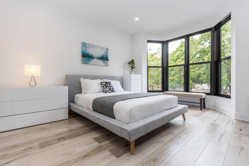 a white bedroom with a bed and a large window at Lofts du Parc LaHaie in Montréal